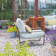 A gravel garden with a greenhouse and the John Lewis Marcy garden chair in green stripe with a matching two-seater outdoor sofa