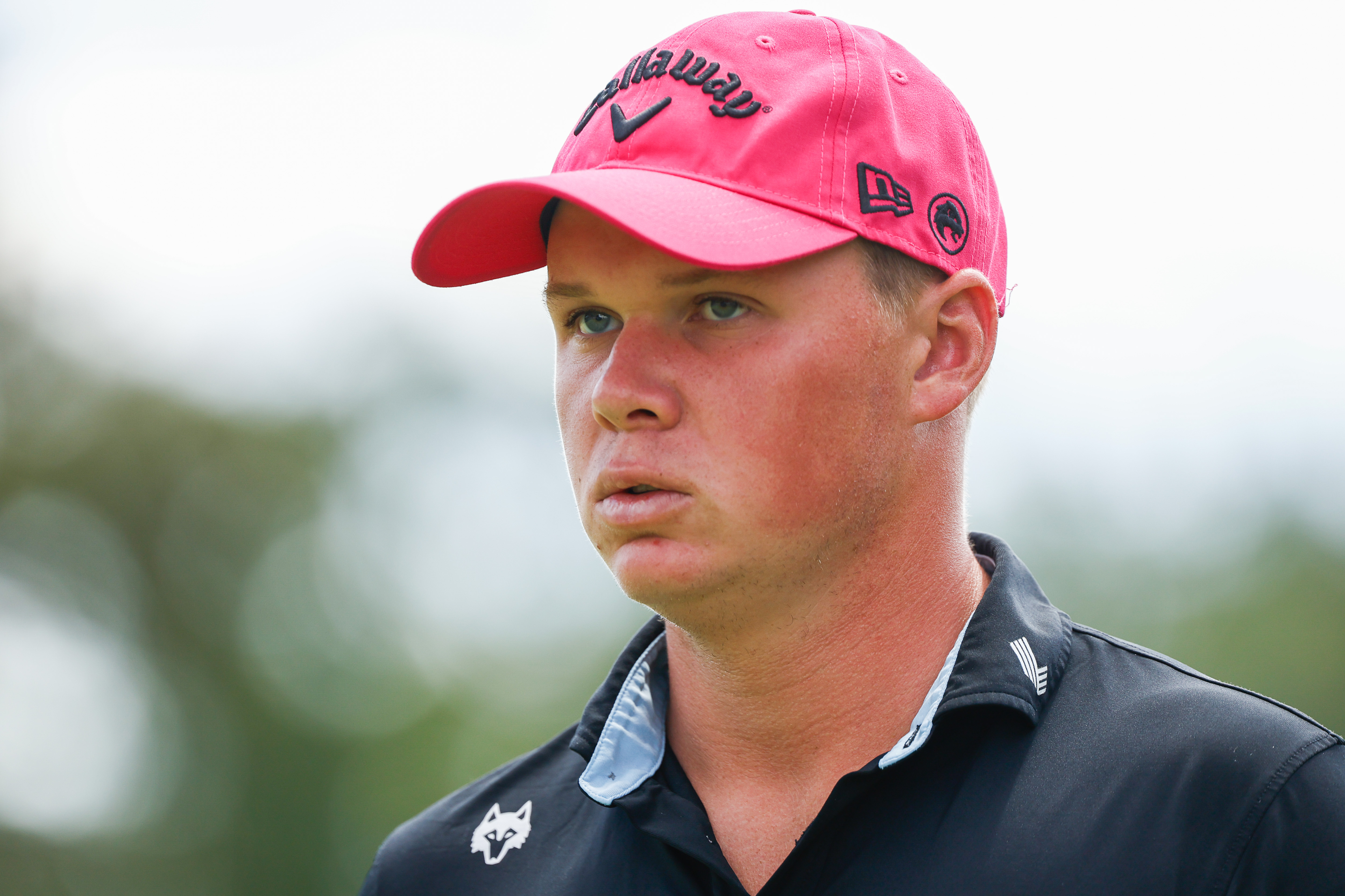 Caleb Surratt wearing a pink cap and black polo during a LIV Golf tournament
