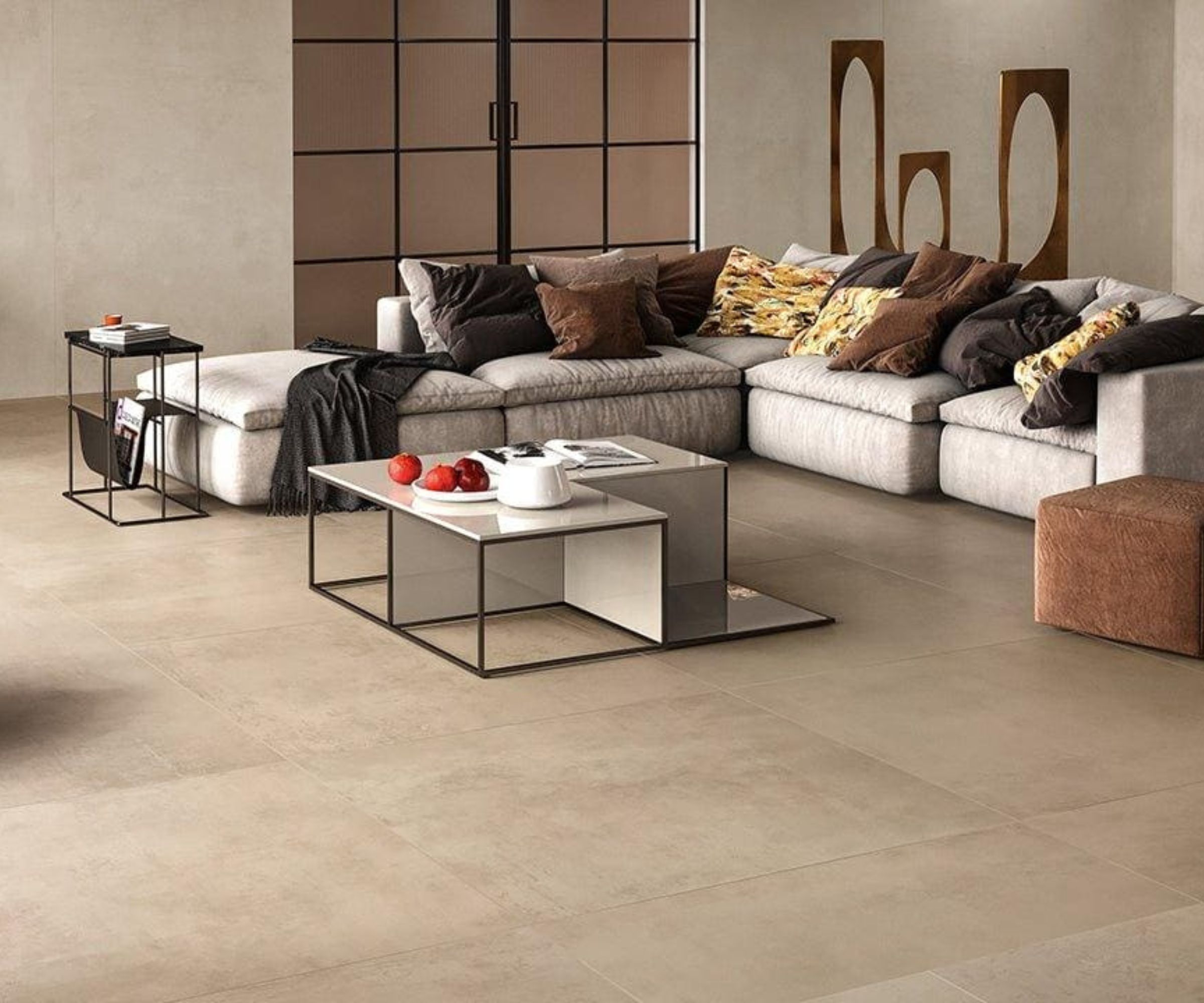 A modern living space with pale stone floor tiles and a low, modular sofa upholstered in light fabric. Neutral cushions add texture. A glass-topped coffee table sits centrally, with minimal side tables and soft lighting creating a calm, uncluttered atmosphere.