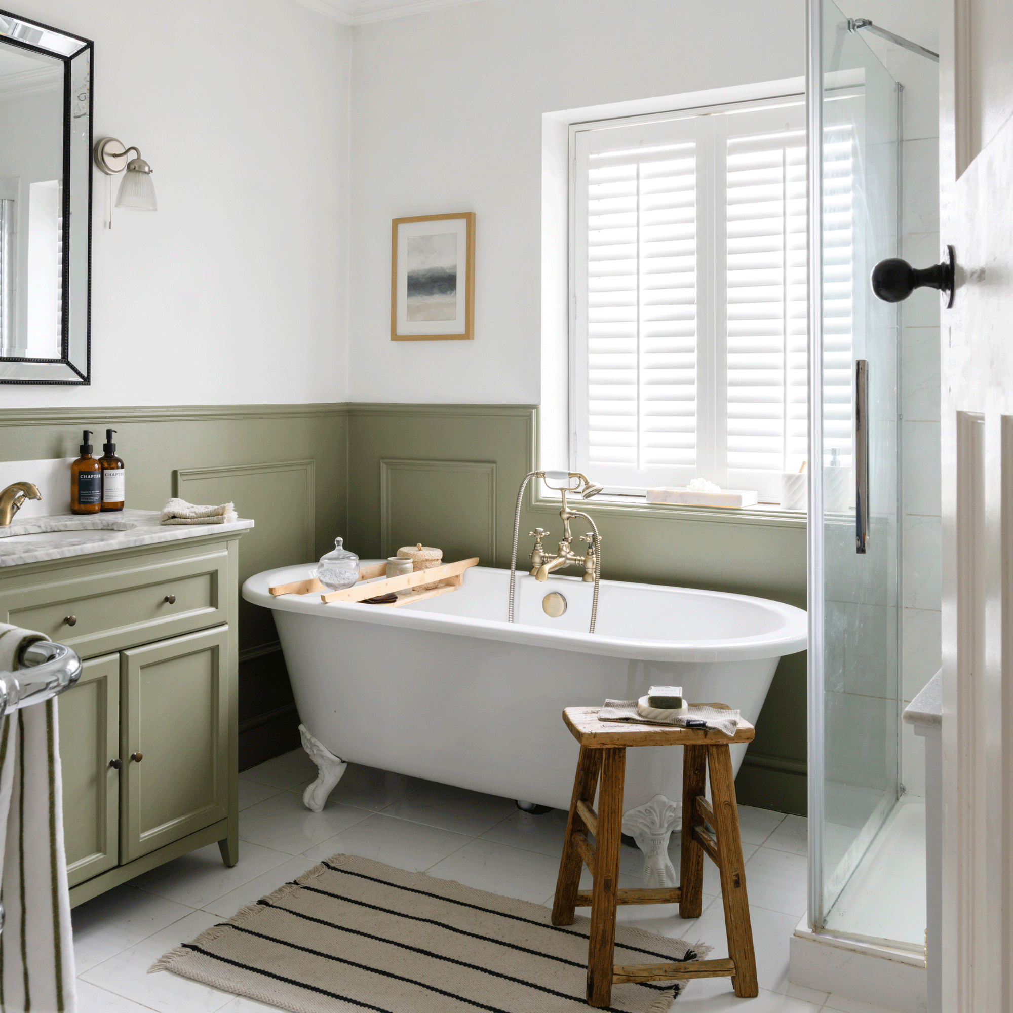 a green and white bathroom with a freestanding bath, green wall panelling and white window shutters