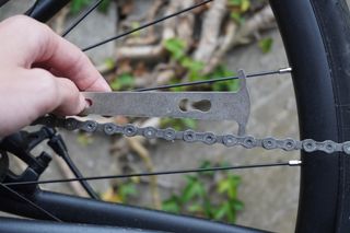 Image shows a person using a chain checker to maintain their bike on a budget.