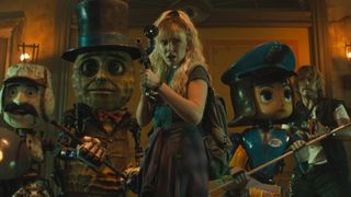 Millie Bobby Brown's Michelle armed with a paint gun while standing next to some robots in Netflix's The Electric State movie