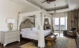Park Hyatt hotel room with four poster canopy holding mosquito net, oriental foot bench, Persian carpet and wooden ceiling fan