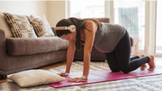 woman on yoga mat on all fours wearing headphones