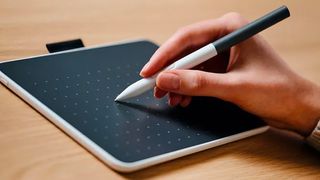 Best drawing tablets; a hand holds a stylus and uses a drawing tablet