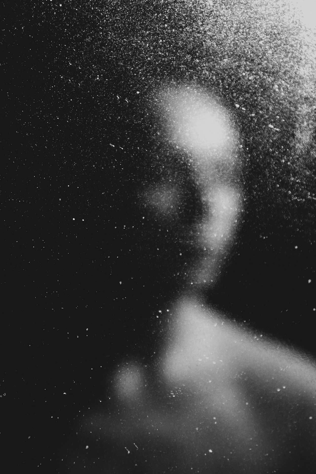 A blurred face is faintly visible through a speckled and lightly fogged glass surface, enhancing the mysterious ambiance