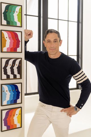 Jonathan Adler stood next to a wall with artwork hung in a vertical row