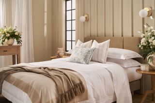 White bed sheets and white striped shams. The set is paired with a camel knit throw blanket and a blue and white printed cushion.