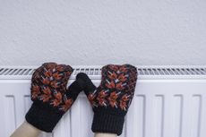 Hands wearing mittens resting on a radiator