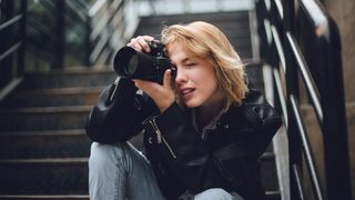 One woman, sitting outdoors on steps, holding a camera.