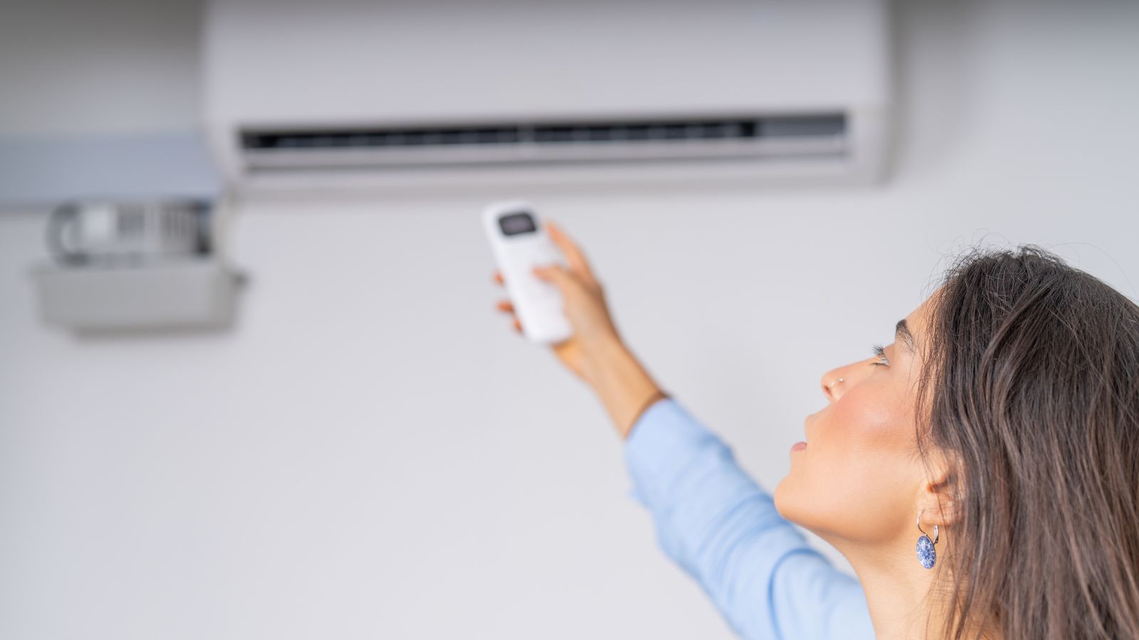 Young woman turning on the air conditioner with the remote control, in the living room