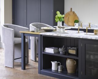 A navy kitchen island setup with luxury grey velvet bar stool, marble kitchen countertop and brass faucet fixtures