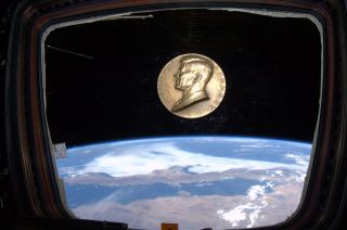 A bronze medallion emblazoned with the likeness of President John F. Kennedy floats on the International Space Station.