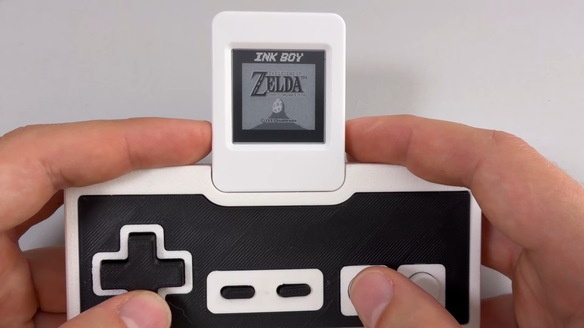 Hands holding Ink-Boy docked on NES controller with Zelda: Link's Awakening on screen.