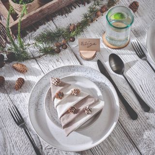 A rustic wooden dining table set for a Christmas dinner with a napkin folded into the shape of a Christmas tree