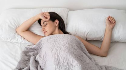 A woman sleeping on a pillow under a duvet with her arms above her head