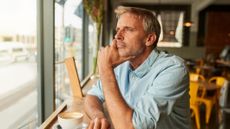 A man in his late 40s or early 50s sits alone in a cafe, looking out the window. He could be lonely, bored or just thoughtful.