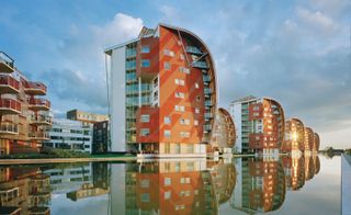 A row of modern-looking buildings painted orange and curved to one side, which looks out to the river.