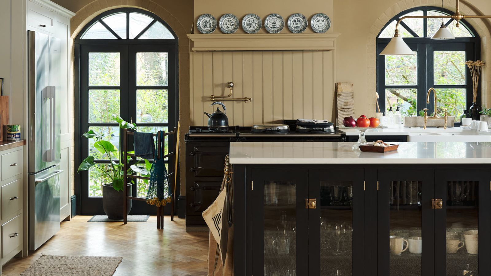 Bright deVOL kitchen with black arched crittal windows and paneled walls, with plate decor on wall and island with white quartz top and parquet floors