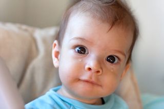 Close-up of a baby crying, with a tear streaming down his cheek.