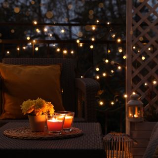 Cosy garden lighting hanging from tree with table and metal chairs next to brick wall of house