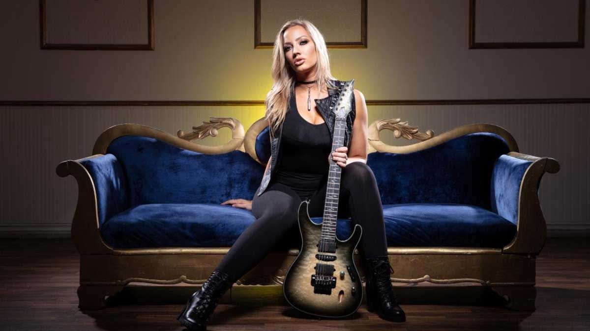 Nita Strauss on a sofa holding a guitar