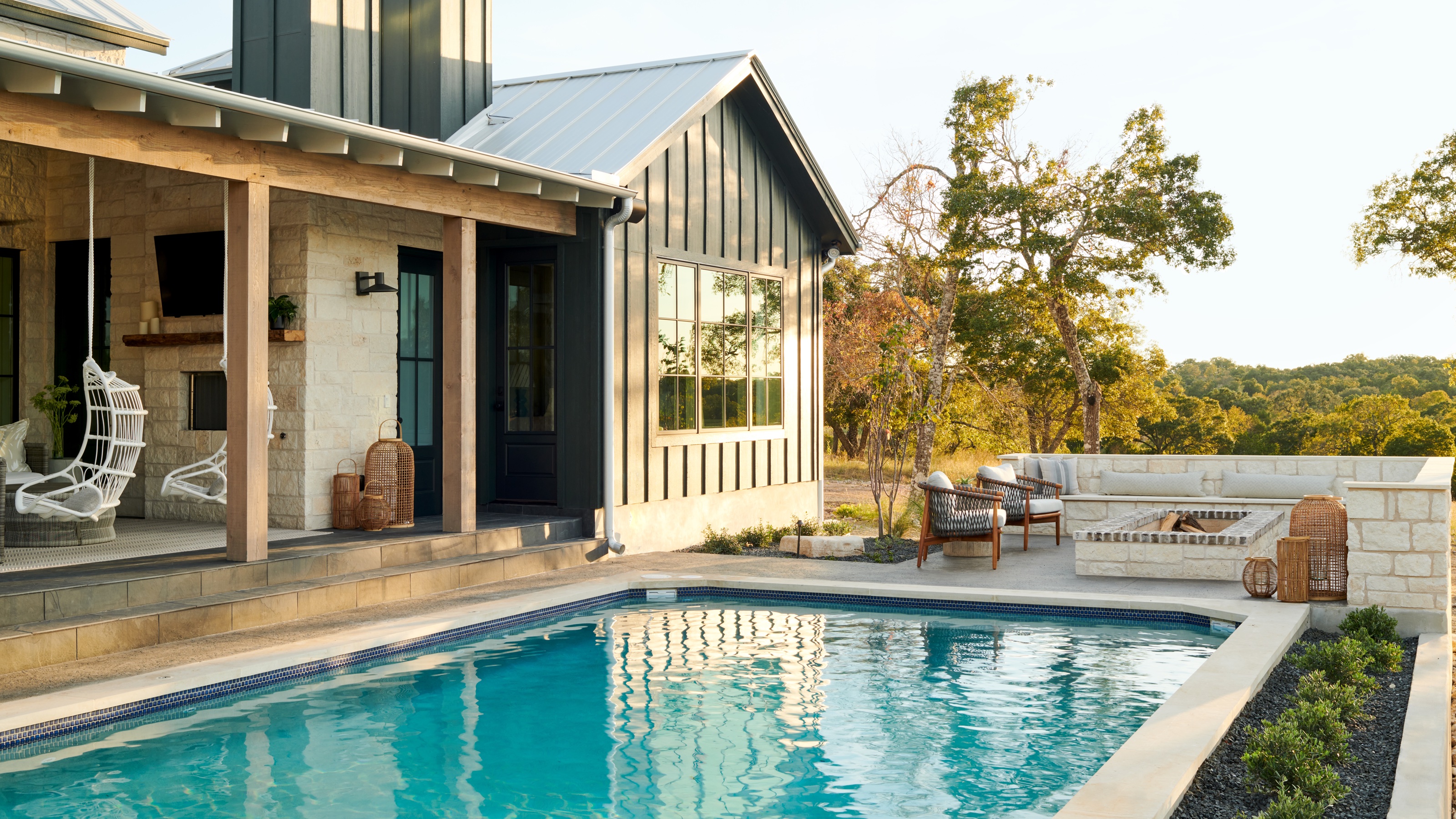 A large outdoor swimming pool with outdoor furniture as well as a firepit. There is also a few of the homes outdoor extension with two lounge chairs hanging 