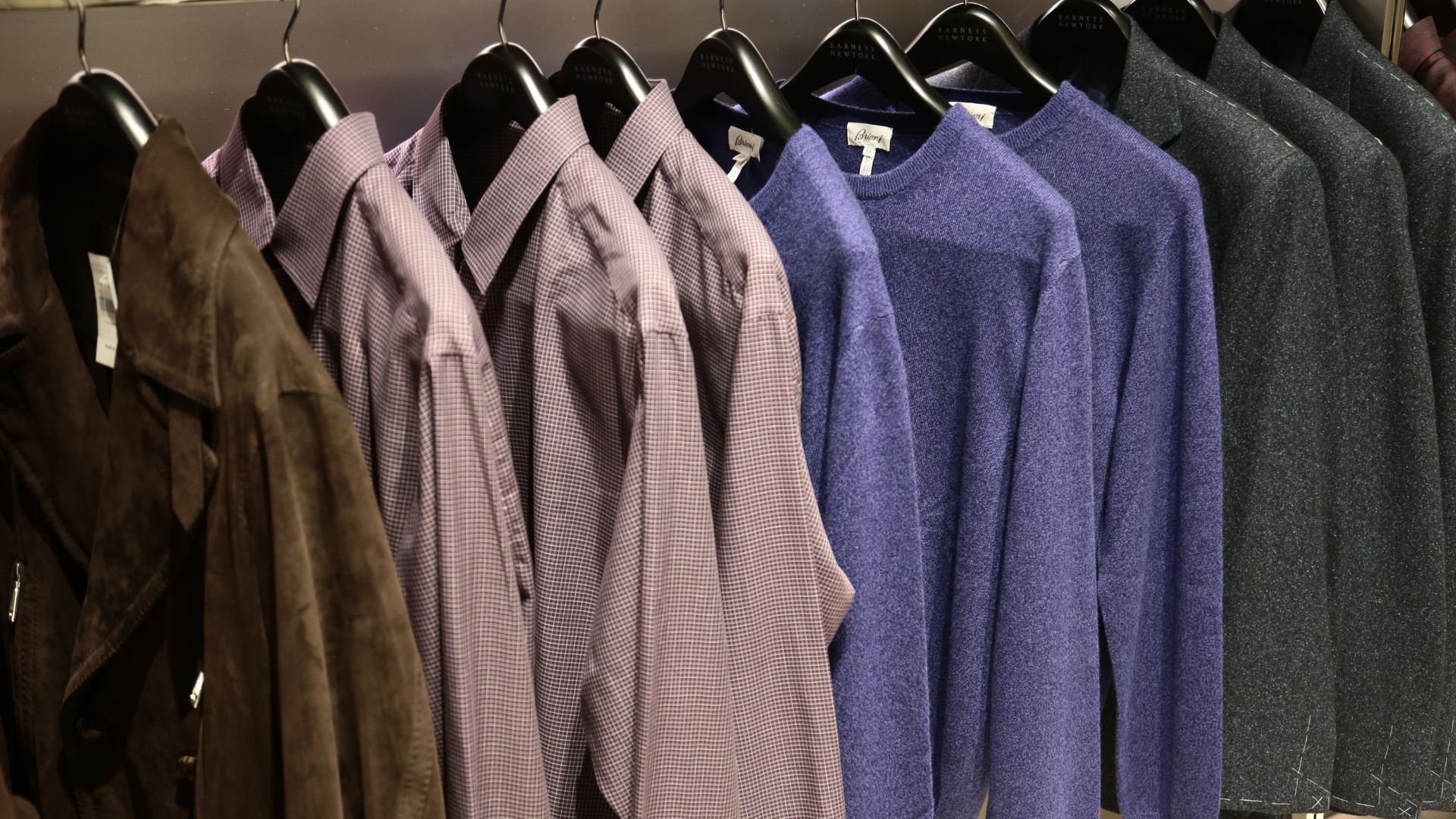 an image of Barney's New Men's Floor with a brown jacket, a red-purple checked short, a purple jumper and a slate blazer on one rack. 