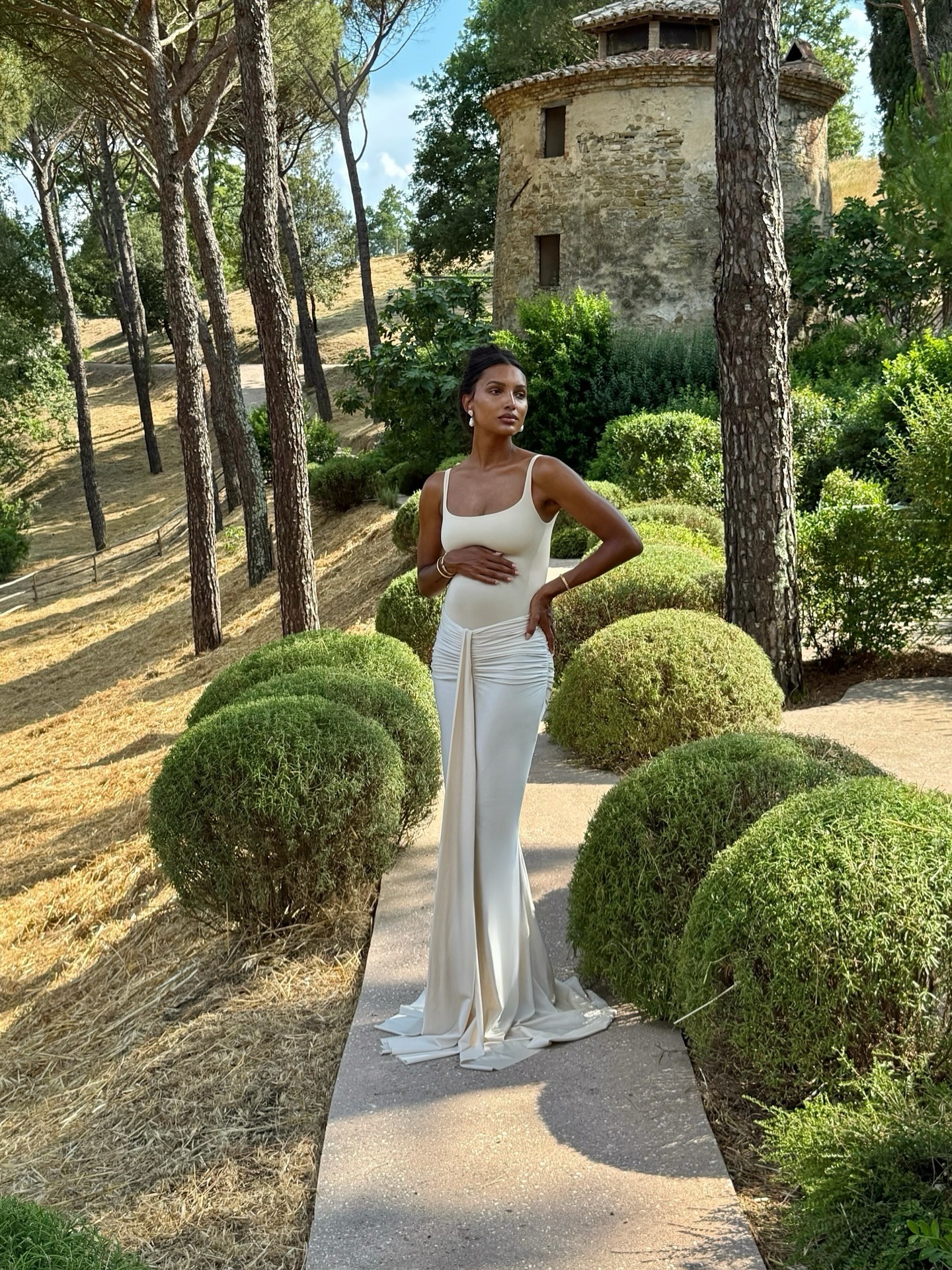 A photo of Jasmine Tookes in a white dress standing amongst a garden in the evening light