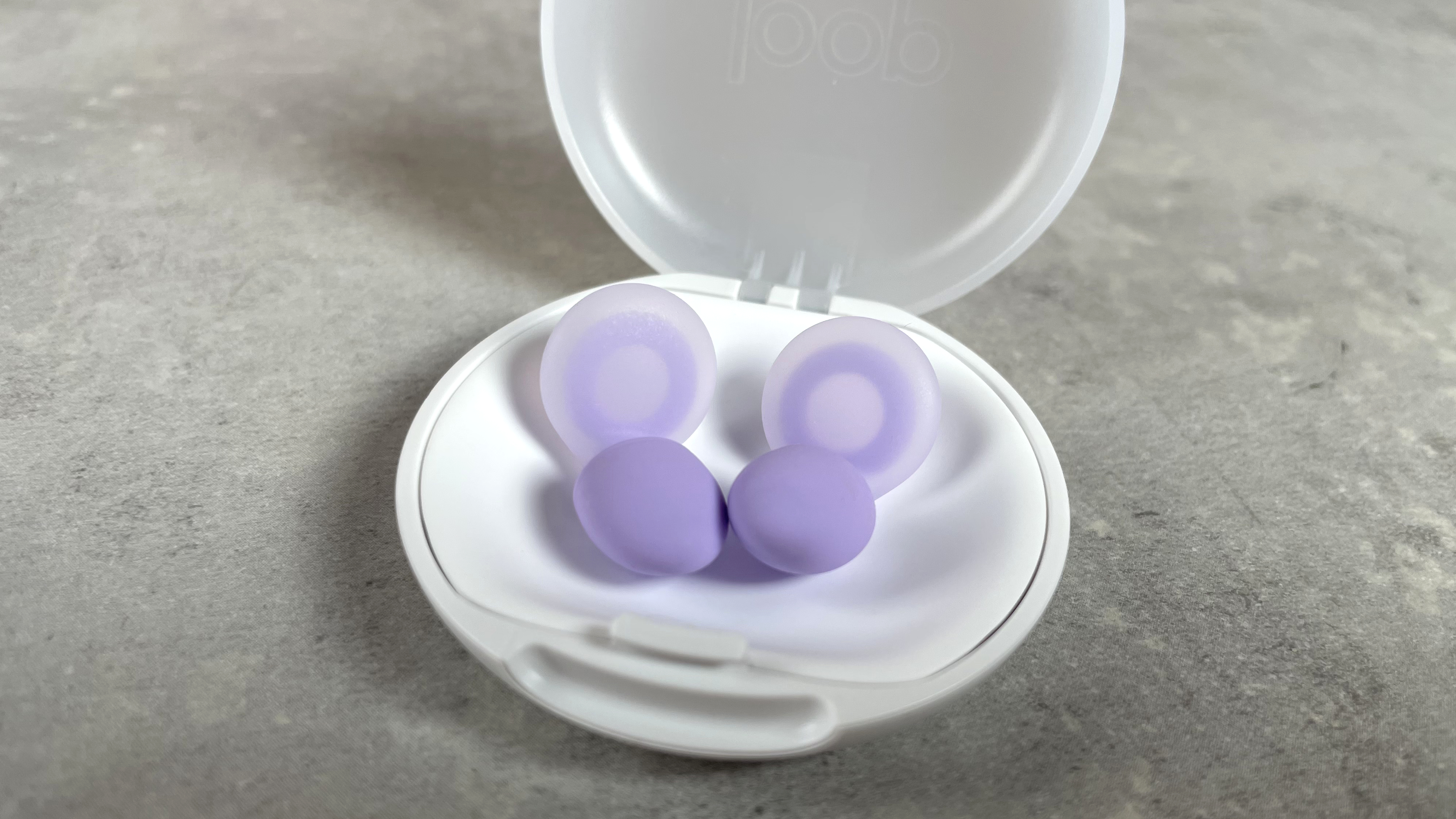 The ear tips and inside of a lilac pair of Loop Dream earplugs, which are sitting in their case.