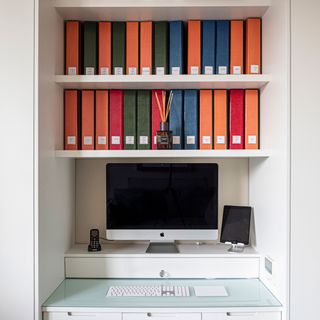 Home office built into small alcove, with shelving for files and riser for monitor