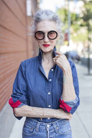 A photo of Linda Rodin in an over 60 outfit featuring a denim button-down shirt and high-waisted blue jeans.