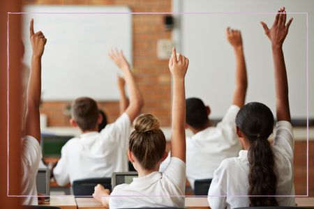 Children sat at their desks with hands raised