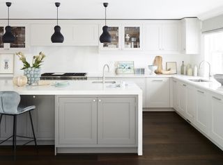 white kitchen with black pendant lights, grey kitchen island, dark wooden floor