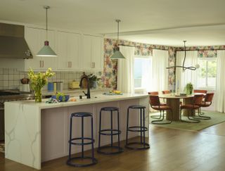 A kitchen with a waterfall island, white cabinetry, and blue bar stools