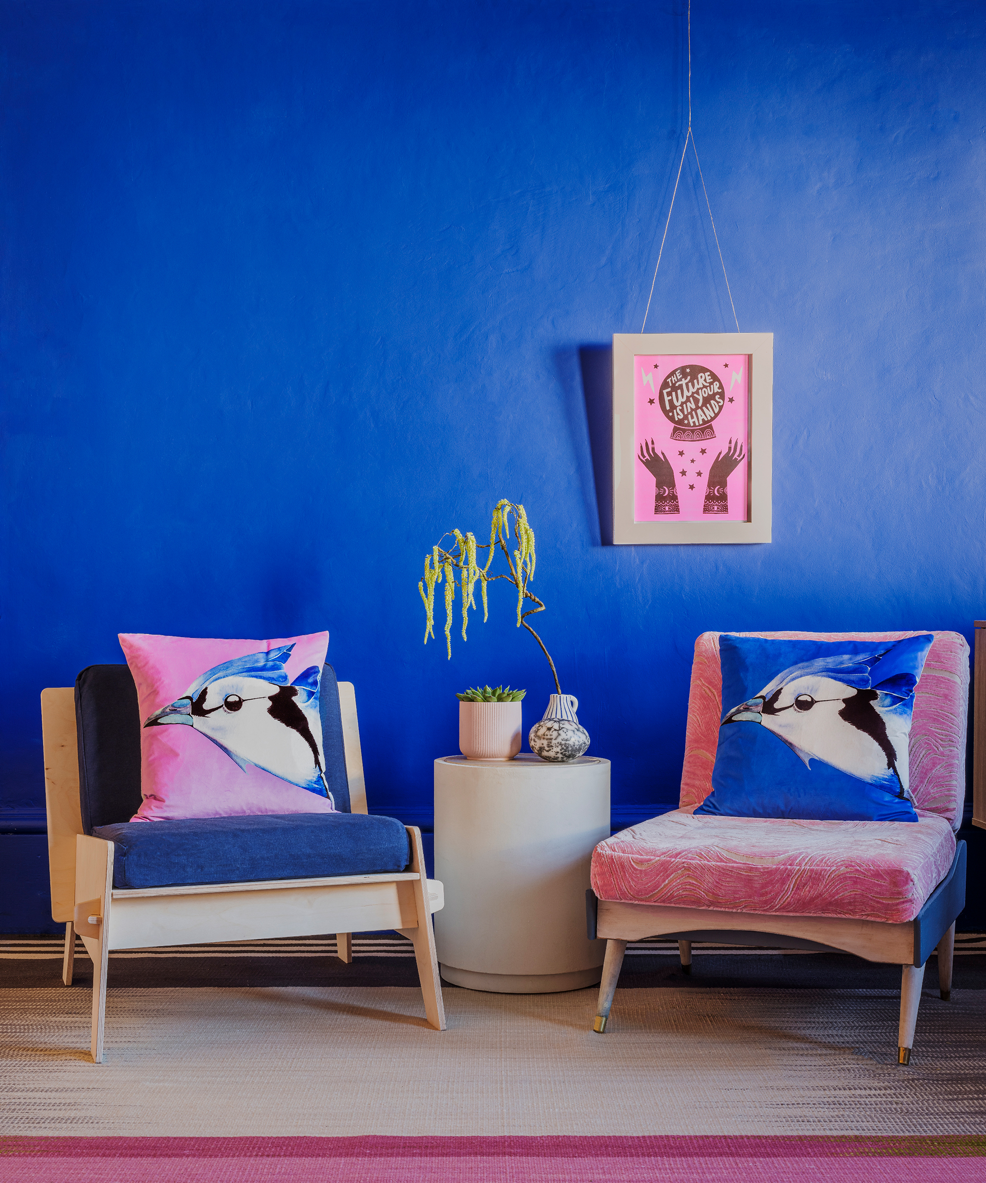 Cobalt blue wall, with pink wall art, and coordinating pink and blue armchairs with bird cushions.