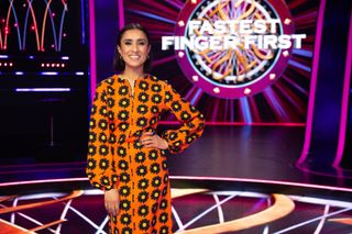 Host Anita Rani in front of the Fastest Finger First logo