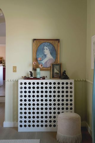 Image of light green bobbin molding across a living room wall. There is a white, modern, circle cut-out console table with a gold framed portrait painting above it.