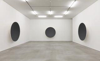 Installation view of ’Gathering Clouds’ at Kukje Gallery. A view of three white walls with a round black object on each.