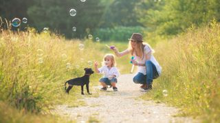 Woman and child blowing bubbles outside with dog