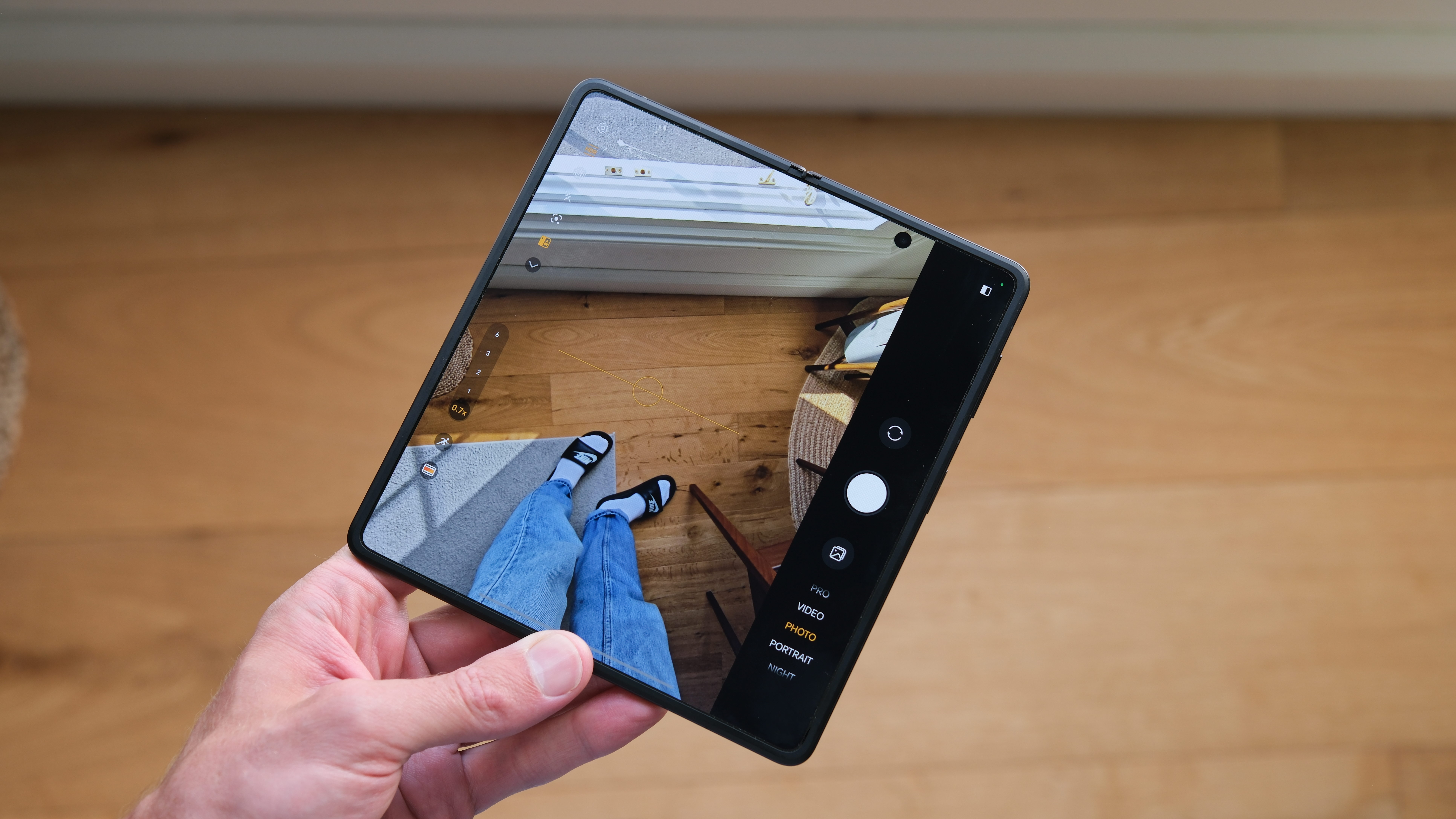 Honor Magic V5 folding phone held in a hand, showing the camera app pointing at the photographer&#039;s legs