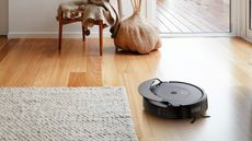 The Roomba Combo® 10 Max robot on a wooden floor next to a flat weave wool rug. 