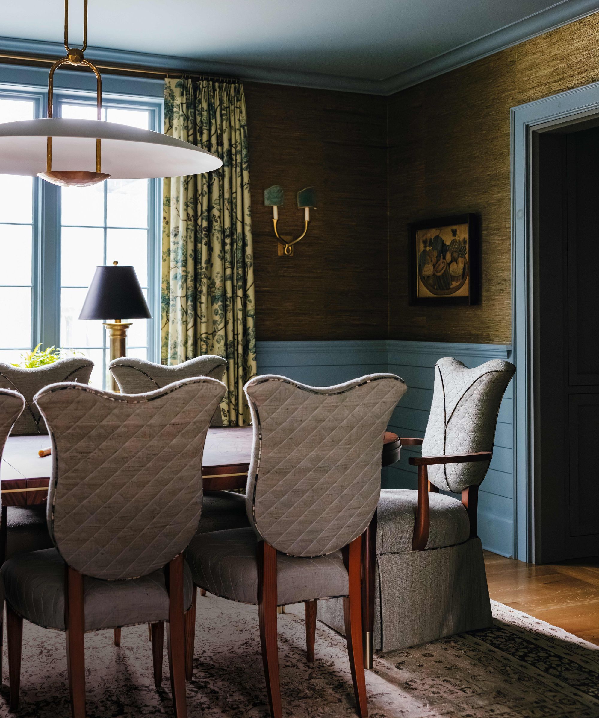 a blue painted dining room with half height paneling and grasscloth walls, with tulpi shaped chairs and wooden table