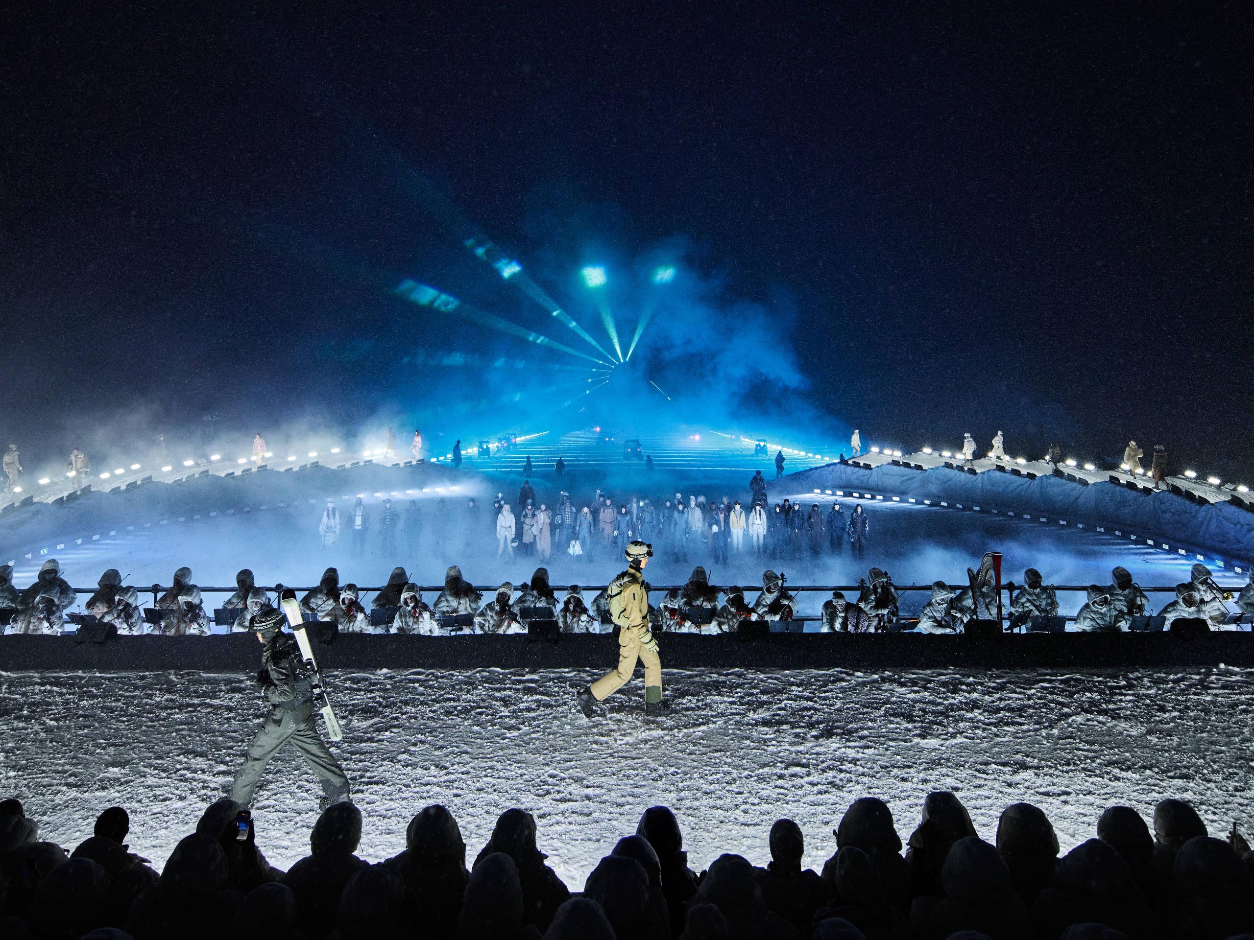 Model wearing Moncler Grenoble technical winter clothing on a snowy runway.