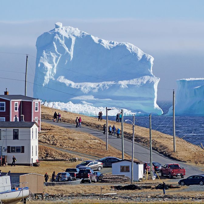 An iceberg dwarfs a Newfoundland coastal village A massive iceberg towering beside a small Newfoundland coastal community