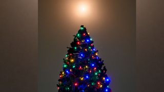 a bright ball of light illuminates the sky above a cone-shaped evergreen tree covered in colored light bulbs