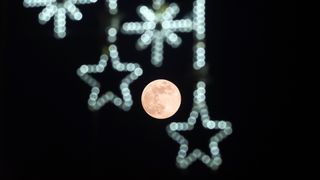 a bright full moon framed by out-of-focus star-shaped holiday lights in the foreground