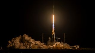 a black-and-white spacex falcon 9 rocket launches into a night sky.