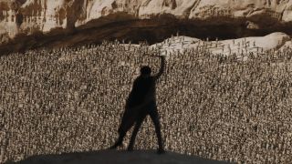 Image from the sci-fi movie Dune. Paul Atreides is holding a sword in the air as he is standing high above a crowd of thousands of people.