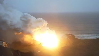 a bright explosion along seaside cliffs next to the ocean on a cloudy, rainy day